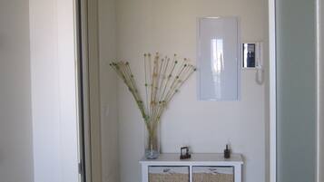 Un couloir avec une console blanche, des paniers en osier et un vase contenant des plantes séchées.