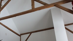 Una habitación con vigas de madera a la vista, un taburete de madera con asiento de piel y un sofá de cuero marrón.