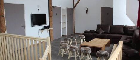 Een ruime woonkamer met een bruine leren bank, een houten salontafel en diverse rustieke krukken.