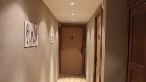 Un pasillo con suelo de baldosas, puertas de madera y cuadros colgados en la pared.