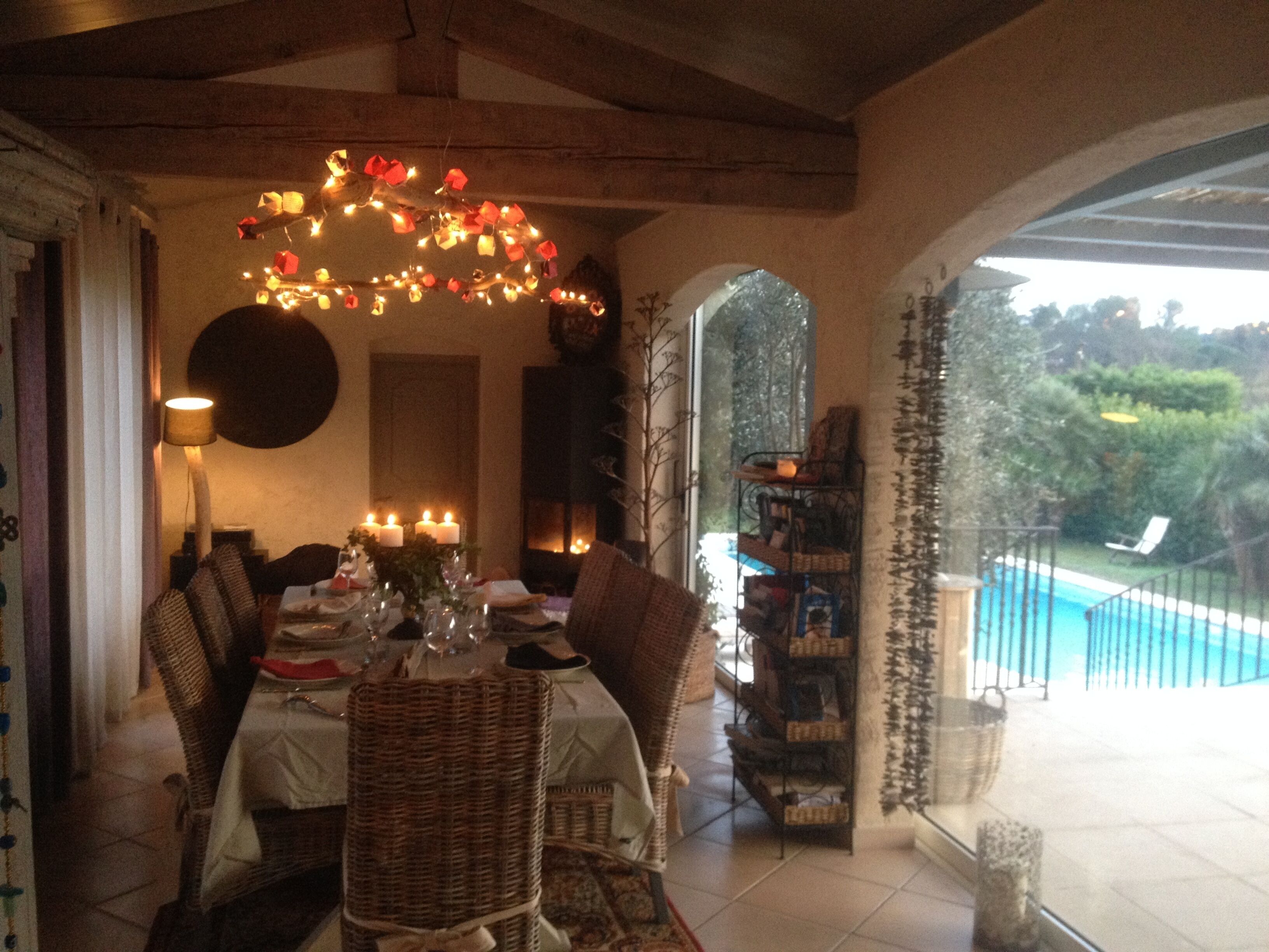 Un coin repas avec une table dressée pour le repas, un lustre et une vue sur une piscine.