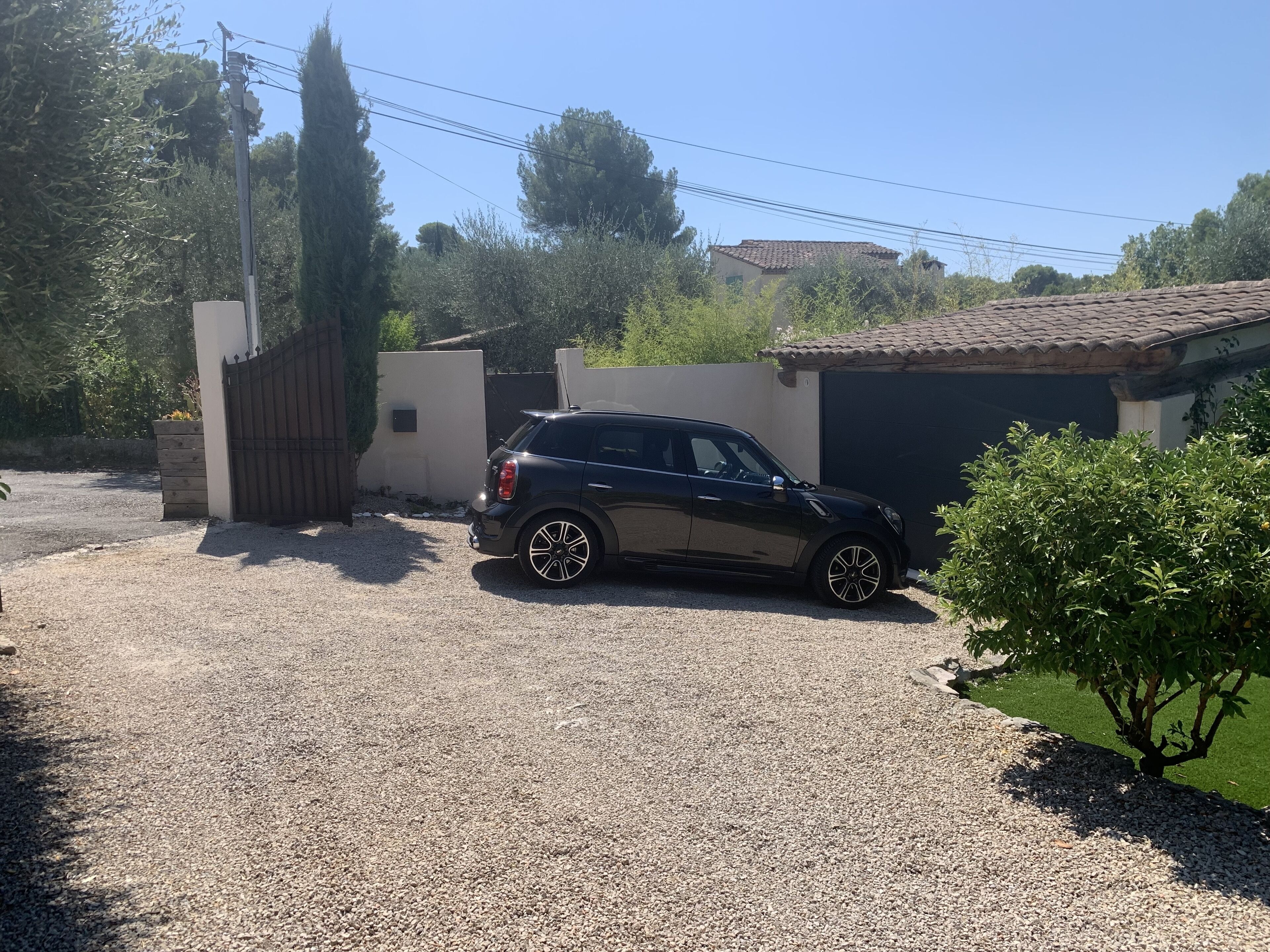 Um SUV preto estacionado em uma entrada de garagem com piso de cascalho, um portão e um pequeno galpão ao fundo.