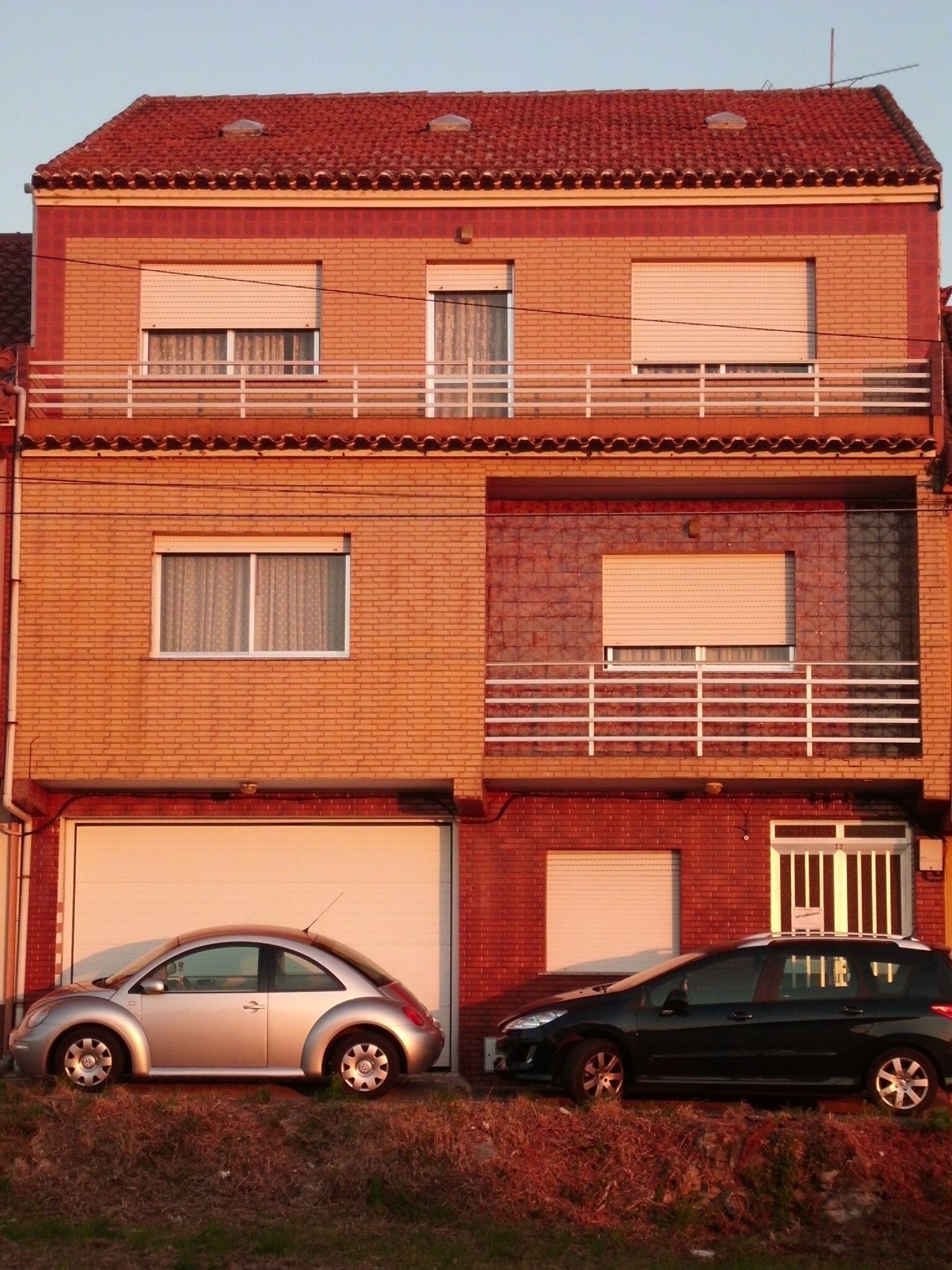 A two-story building with a garage, two cars parked in front, and a balcony on the upper floor.