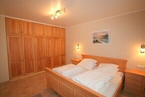 A bedroom with a wooden bed, a wardrobe, and two bedside lamps. - House beacon apartment 2, no smoking, balcony (Cuxhaven)