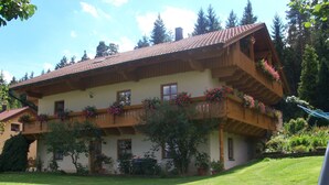 A two-story chalet with balconies adorned with flowers, a well-maintained lawn, and a sandbox in the foreground.