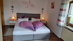 Une chambre à coucher comprenant un lit, des oreillers, des tables de chevet, des éléments de décoration murale et une fenêtre avec des rideaux.