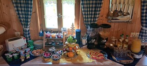 Un bufé de desayuno con diversos alimentos y bebidas, un tostador y utensilios de cocina sobre una mesa de madera.