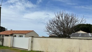 A residential area with a house featuring a tiled roof, a white gate, and a tree with bare branches.