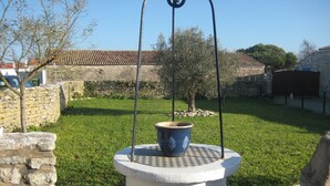 A courtyard with a stone well, a tree, and a stone wall.