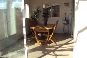 Ein Holzespeisesaal mit Stühlen, einer Blumenvase und einem Topfpflanzen in einem sonnendurchfluteten Zimmer mit Blick ins Freie.