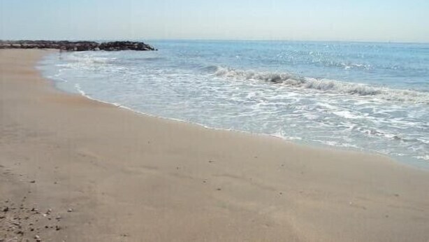 Ein Sandstrand mit sanften Wellen und blauem Himmel.