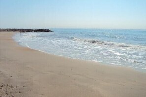 Ein Sandstrand mit sanften Wellen und blauem Himmel.