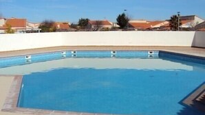 Ein rechteckiger Pool mit Fliesenrand, umgeben von einer niedrigen weißen Mauer und einem beigefarbenen Boden.