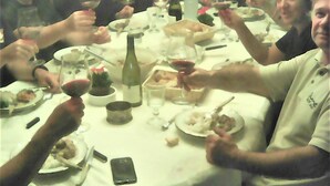 A group of people seated around a round table with plates, glasses, and a bottle, suggesting a dining setting.
