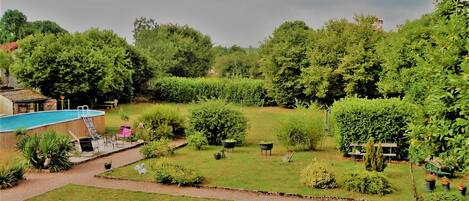 Ein Garten mit Swimmingpool, einer Terrasse mit Stühlen und verschiedenen Pflanzen.