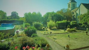 A garden with a swimming pool, a church, and various plants.