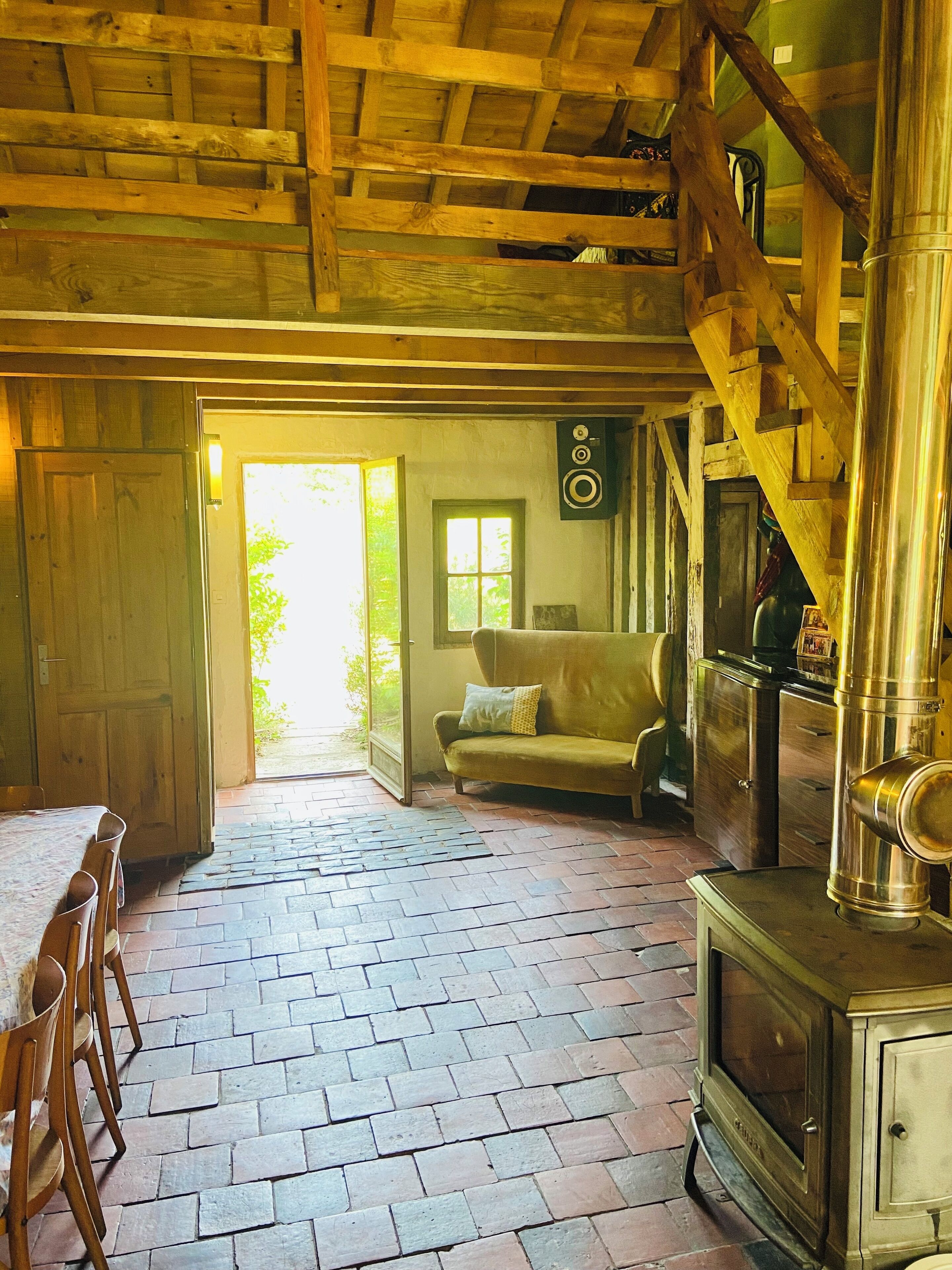 A rustic wooden interior with a brick floor, a sofa, a dining table with chairs, and a vintage stove.