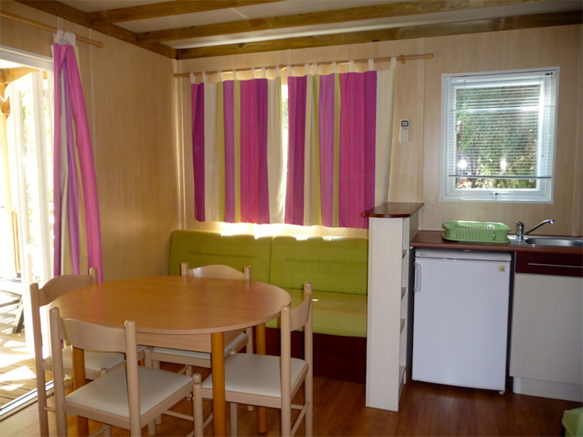 A compact kitchen with a dining area, a green sofa, and a small refrigerator.