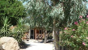 A rustic cabin with a wooden deck, surrounded by large rocks and various trees. - 2/4-person CLIMATIZED WOODEN CHALET CLOSE TO ALGAJOLA village views (Algajola)
