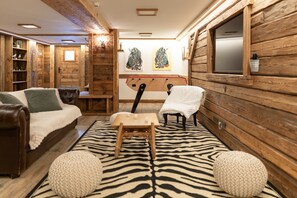 A cozy room with wooden walls, a zebra-patterned rug, a bed, a chair, and a small table.