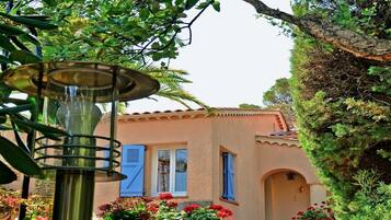 A rustic building with blue shutters, a tiled roof, and a garden with potted plants.