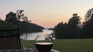 A glass of red wine on a metal table with a view of a lake and trees at sunset. - Lake Front, Walk out ground level, Sunset VIEW, Dedicated Slip, Awesome Pool (Dadeville)