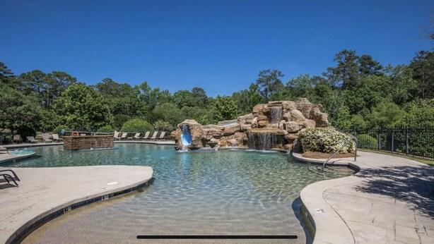 A clear swimming pool with a waterfall feature, surrounded by trees and a stone structure. - Lake Front, Walk out ground level, Sunset VIEW, Dedicated Slip, Awesome Pool (Dadeville)