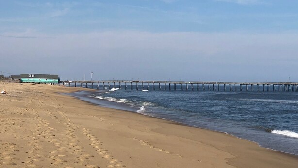 Una spiaggia con un molo che si protende nell'acqua, un edificio con tetto verde e impronte sulla sabbia.