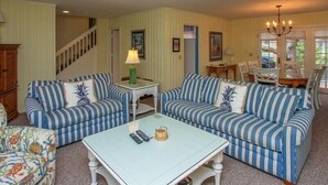 A living room with two striped sofas, a small table, and a staircase. - 4th Row Ocean Home w/ Private Pool (Hilton Head Island)