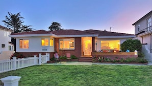 A two-story house with a well-maintained lawn, a white picket fence, and a front porch with outdoor seating. - OCEANFRONT! BEST LOCATION! EXTRAORDINARY VIEWS! HOT TUB! FIRE PIT! (Santa Cruz)
