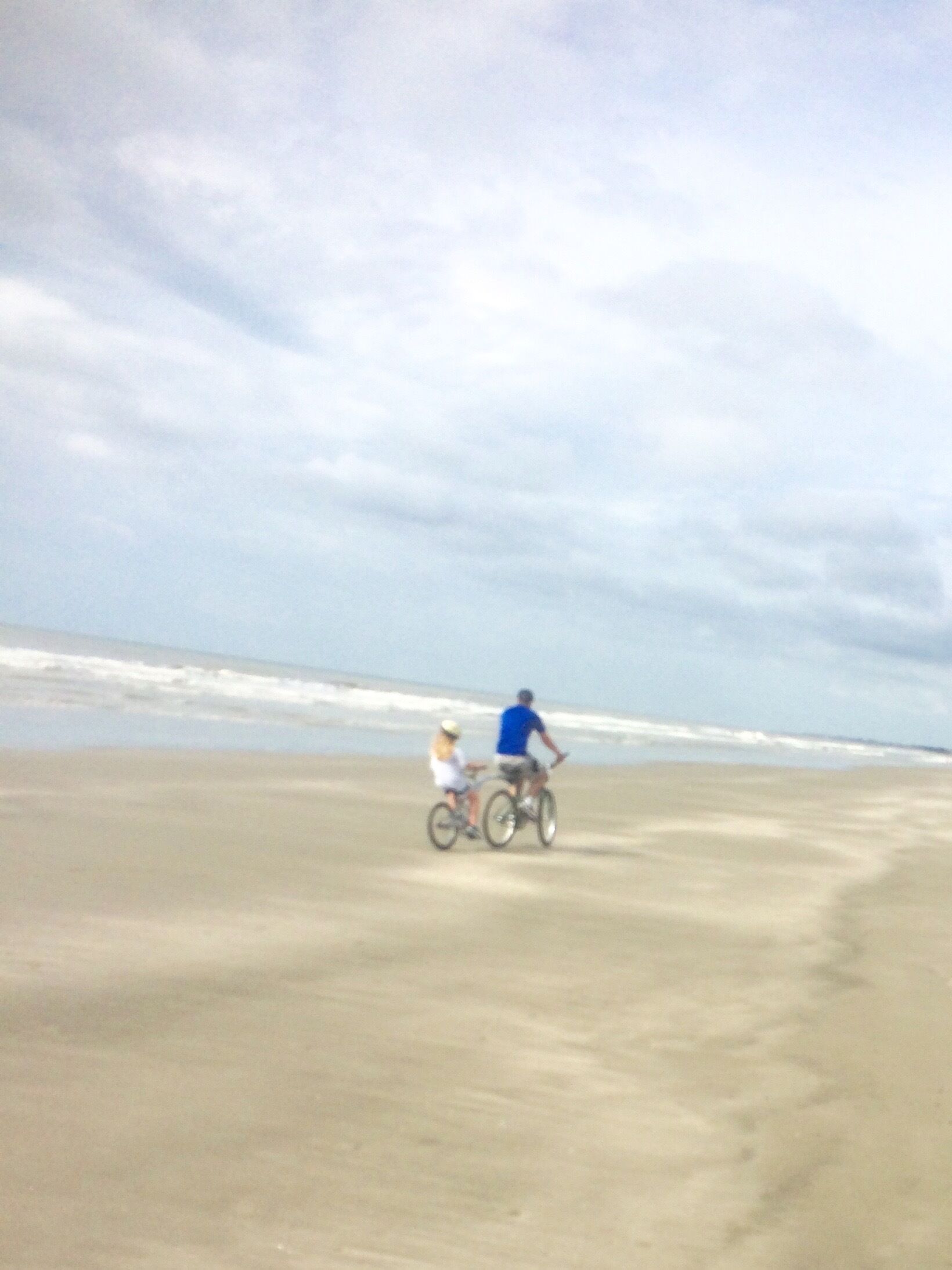 A sandy beach with a person and a child on a bicycle.