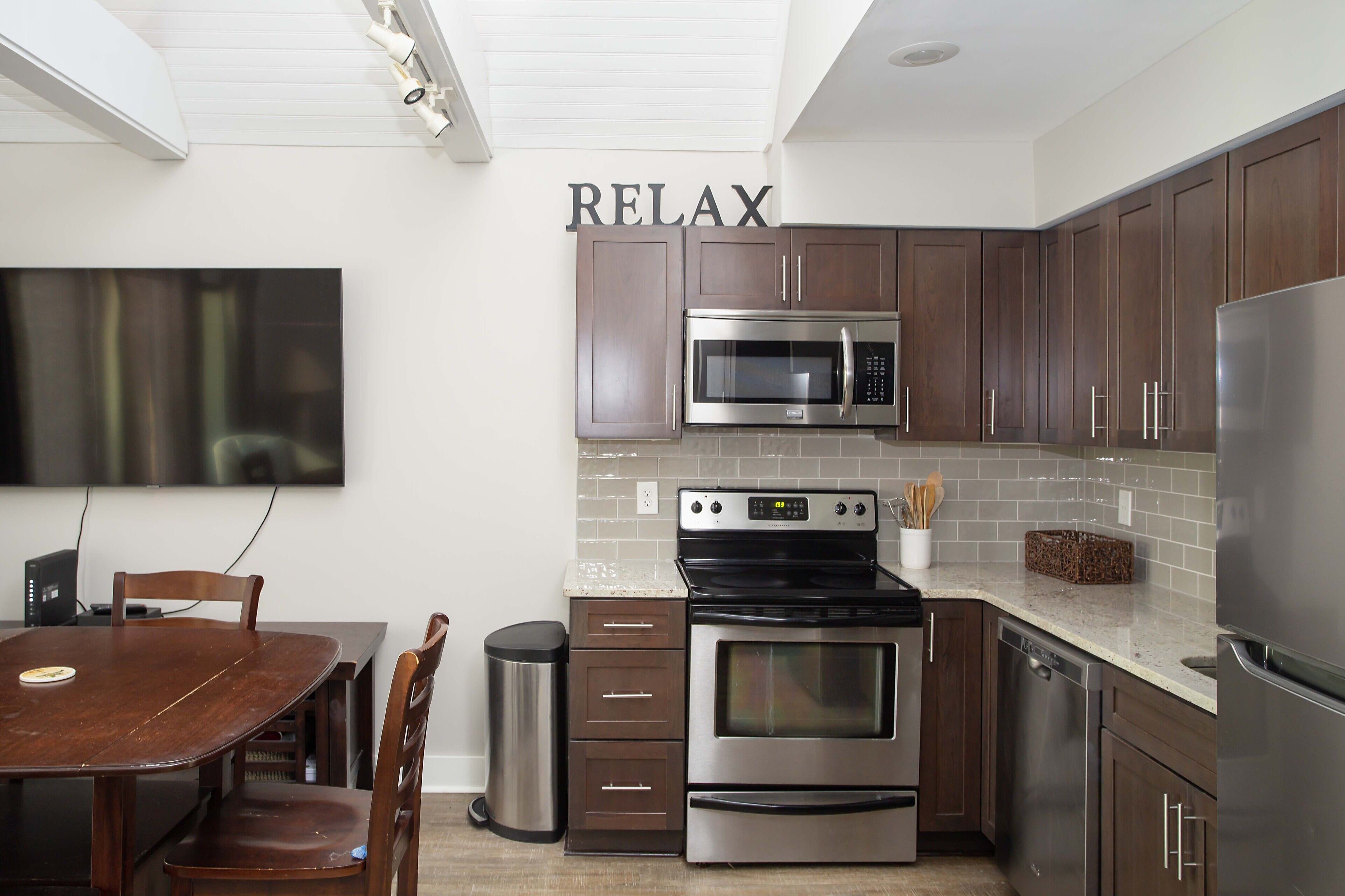 Una cocina moderna con armarios de madera oscura, electrodomésticos de acero inoxidable, una mesa de comedor con sillas y un cartel con la palabra 'RELAX'.