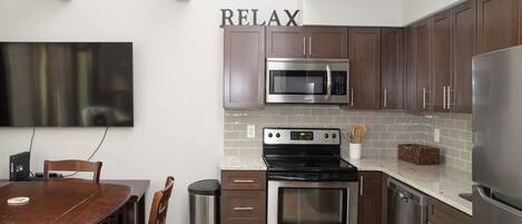 Una cocina moderna con armarios de madera oscura, electrodomésticos de acero inoxidable, una mesa de comedor con sillas y un cartel con la palabra 'RELAX'.