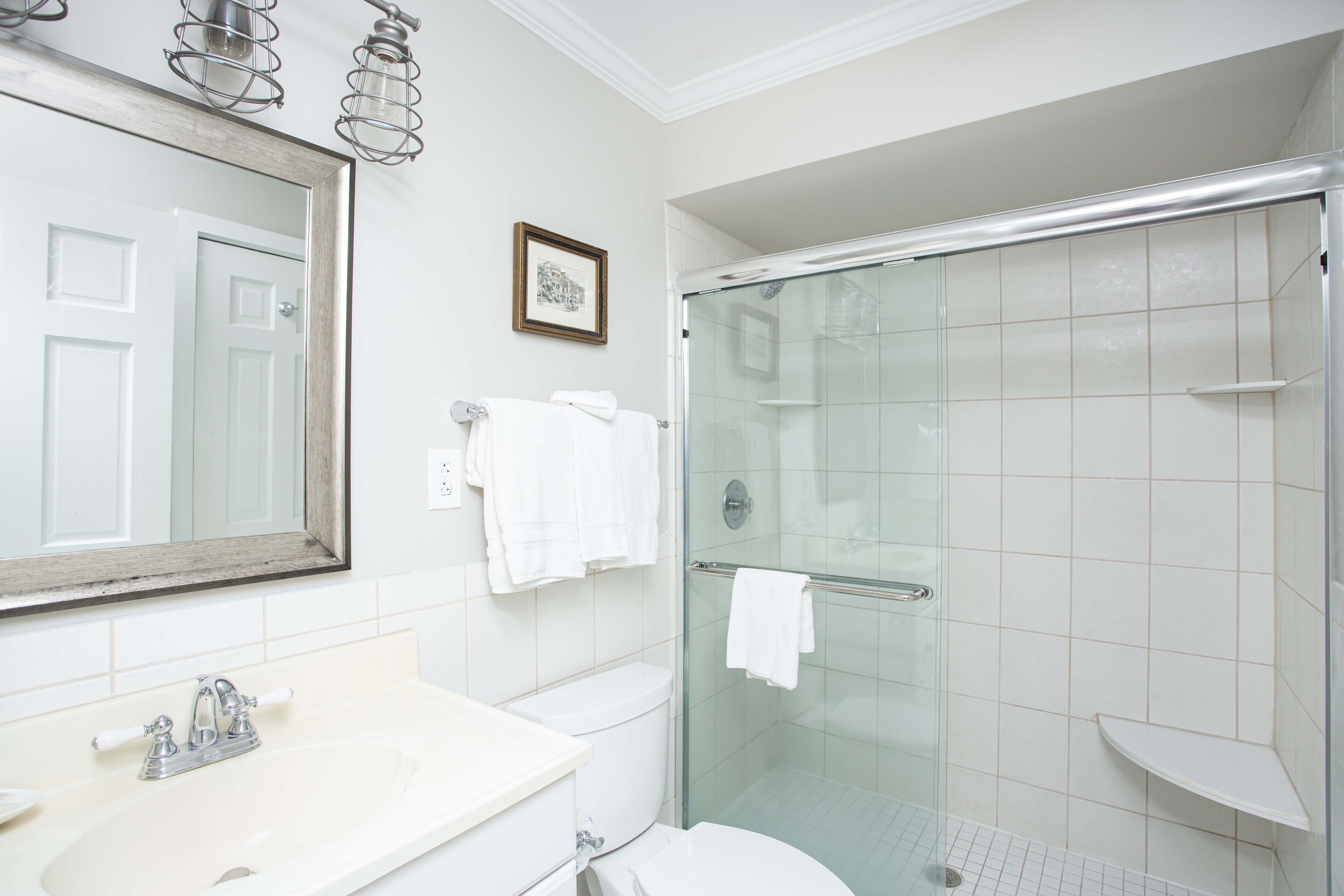 Une salle de bain avec un lavabo blanc, des toilettes, une douche en verre et un grand miroir.