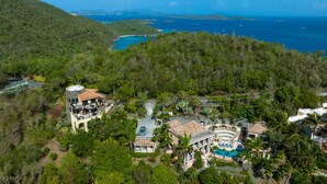 Un gran resort de varios pisos con piscina, rodeado de exuberante vegetación tropical y con vista a la costa.