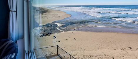 A beach view from a window with a metal railing, a clear sky, and the ocean.