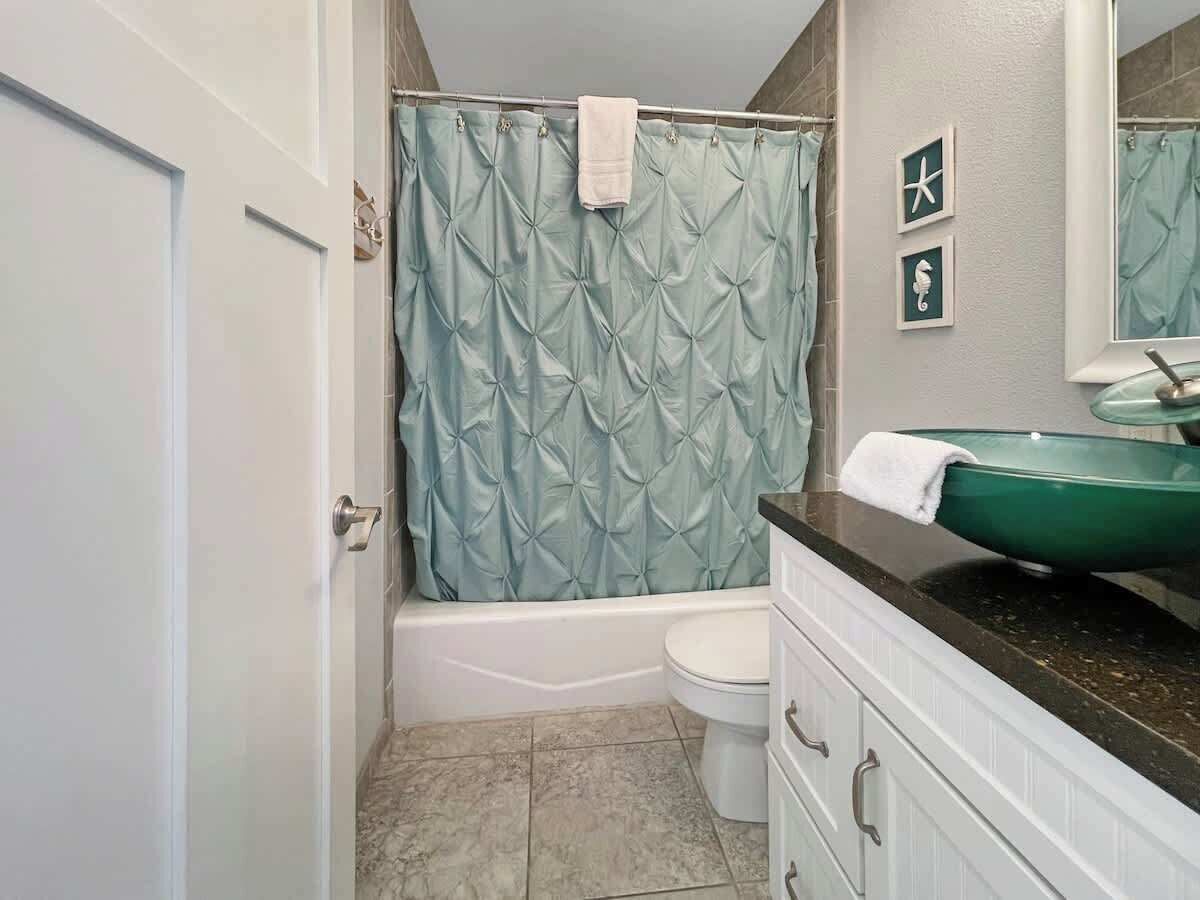 Une salle de bain avec un rideau de douche, des toilettes, un lavabo avec un receveur vert et un miroir.