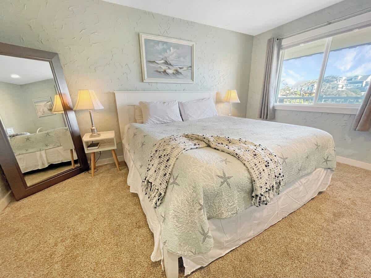 A hotel room with a large bed, a bedside table with lamps, a mirror, and a painting on the wall.