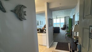 A spacious living area with a kitchen in the background, a ceiling fan, and a view of the ocean.