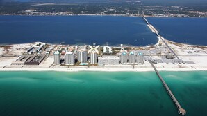 An aerial view of a coastal area with a marina, several high-rise buildings, and a long pier extending into the water.