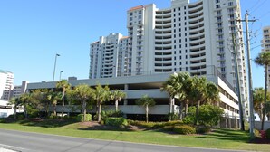A multi-story parking garage with a white exterior and red roof, surrounded by palm trees and greenery.