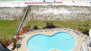 A large, circular swimming pool with sun loungers and umbrellas, surrounded by a deck with a railing.