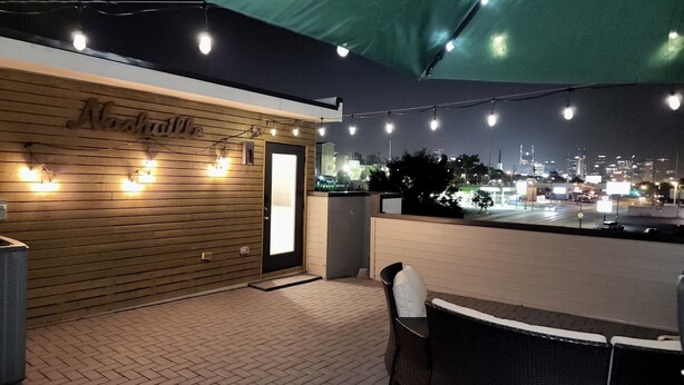 An outdoor seating area with a wooden wall, string lights, and a view of the city at night. - Amazing Location with Private Rooftop (Nashville)