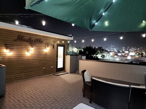 Un espace extérieur aménagé avec des sièges, un mur en bois, des guirlandes lumineuses et une vue sur la ville la nuit.