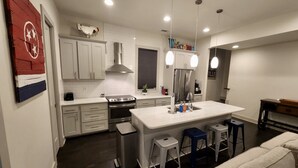 A modern kitchen with white cabinets, stainless steel appliances, and a central island with bar stools. - Amazing Location with Private Rooftop (Nashville)