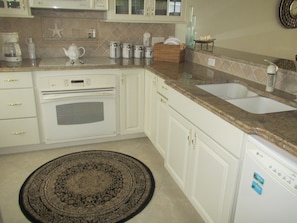 A kitchen with white cabinets, a built-in oven, a sink, and a coffee maker.
