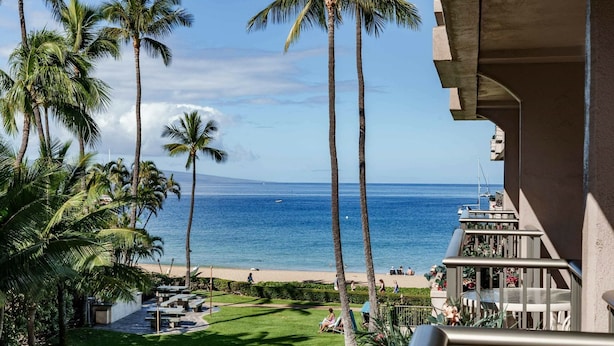 Un balcon avec vue sur la plage et l’océan, des palmiers et des sièges d’extérieur.