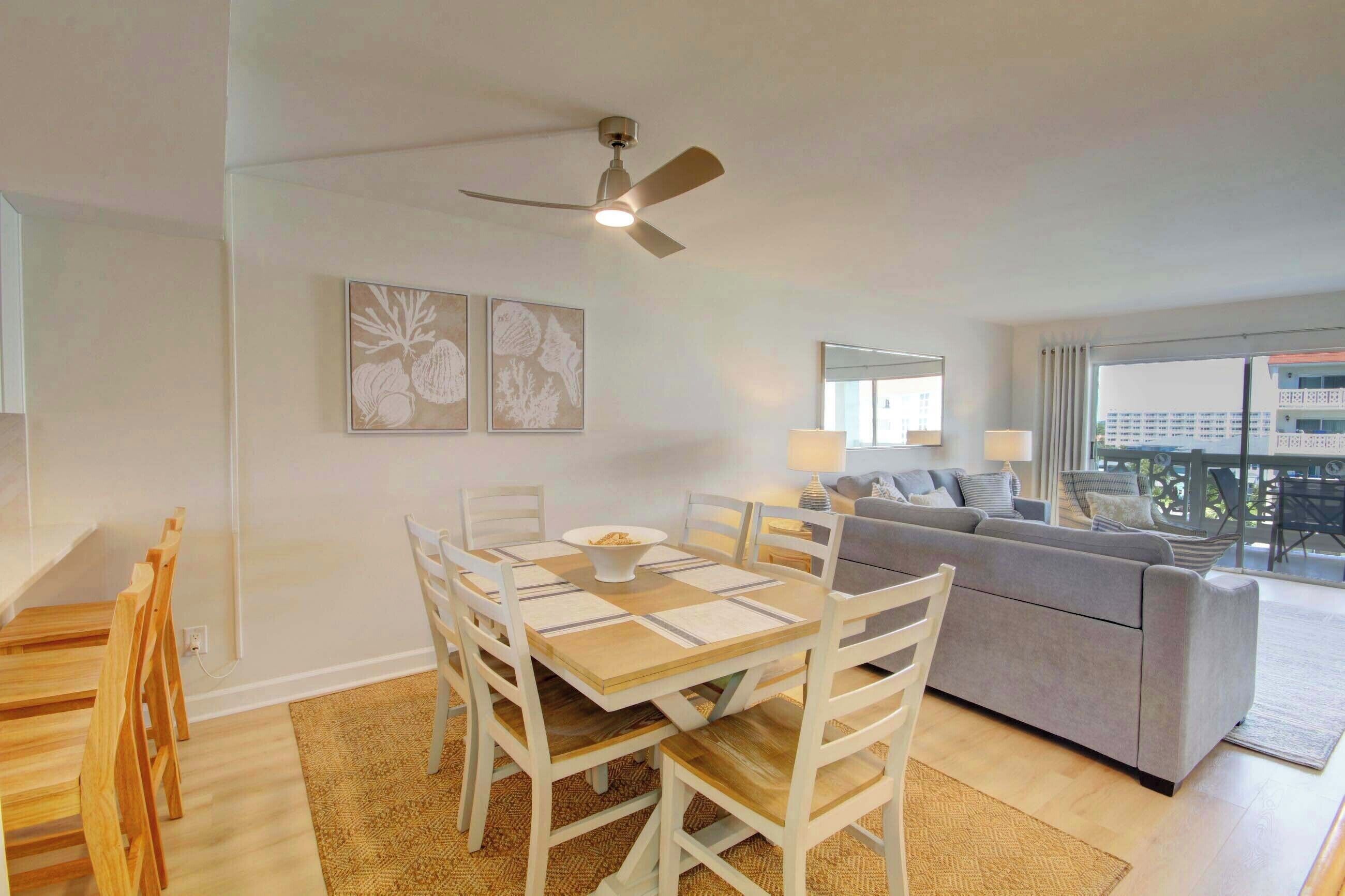 A modern living room with a dining table, chairs, a sofa, and a ceiling fan.
