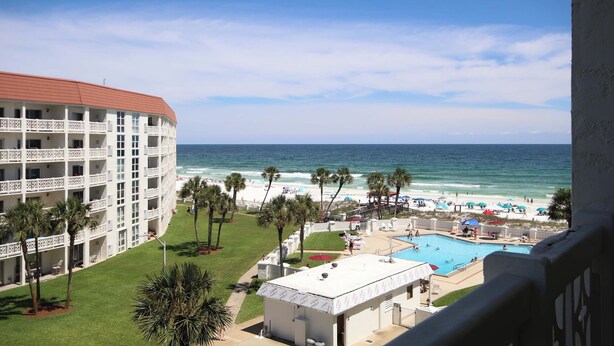 A hotel with a pool, beach view, and palm trees.