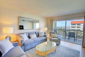 A modern living room with a sofa, armchairs, a glass coffee table, and a balcony with a view.